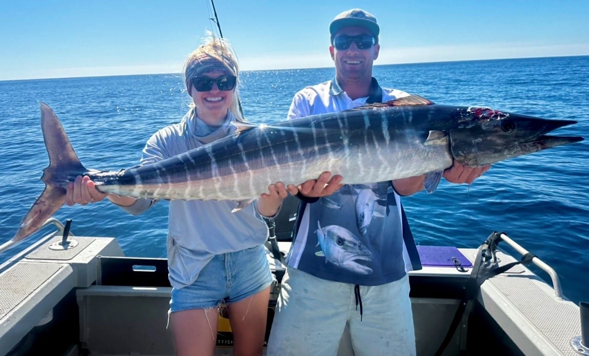 charter guests laura and james holding a big wahoo fish on its side blue ocean in the background