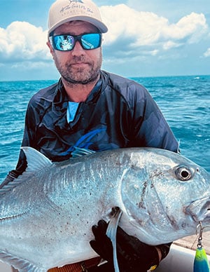 Giant trevally being held by charter guest for a picture before being put back into the water
